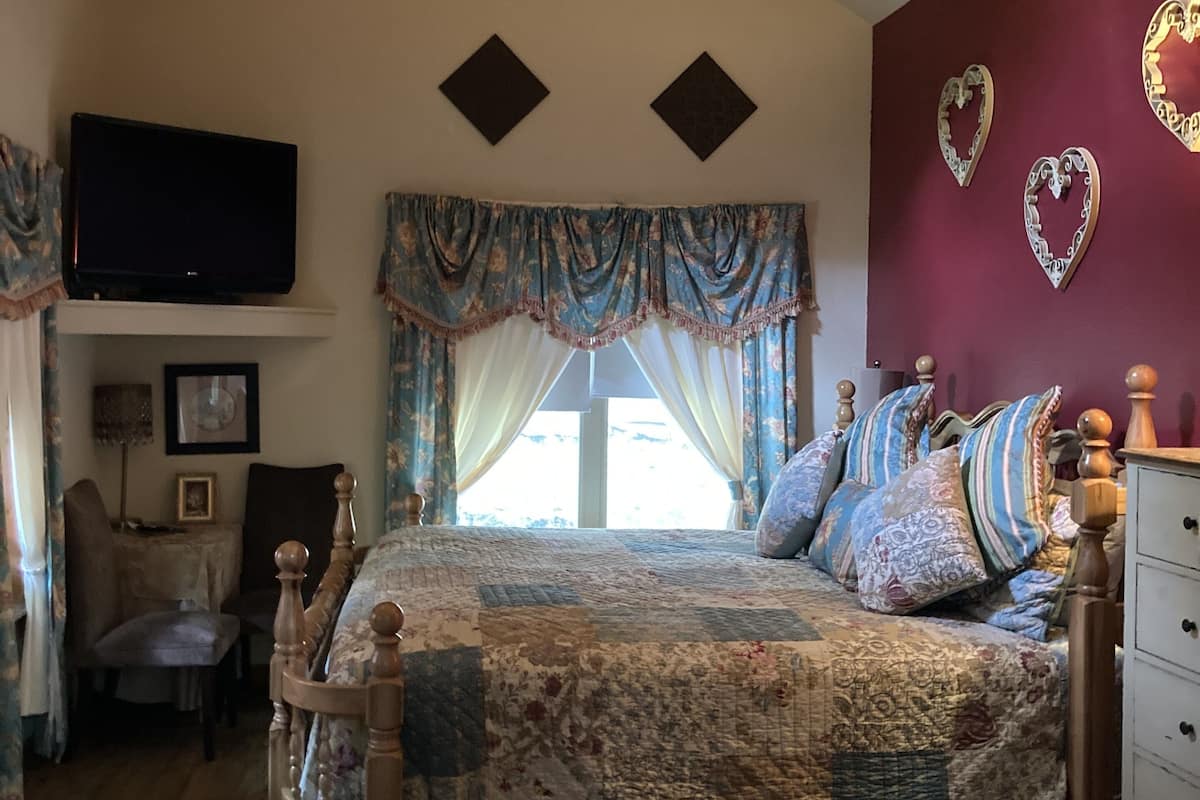 A bedroom with a wooden bed, a TV mounted on the wall, and a window with curtains.