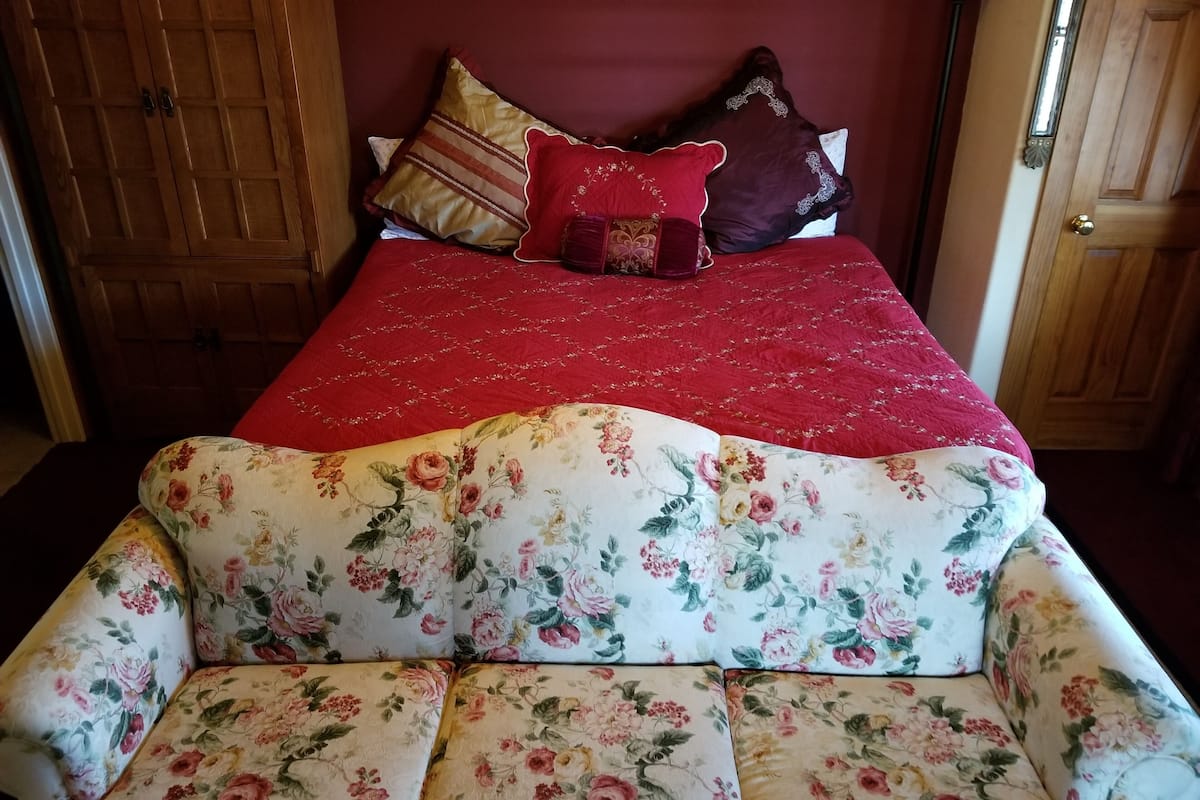 Quarto com sofá floral, colcha vermelha e guarda-roupa de madeira.