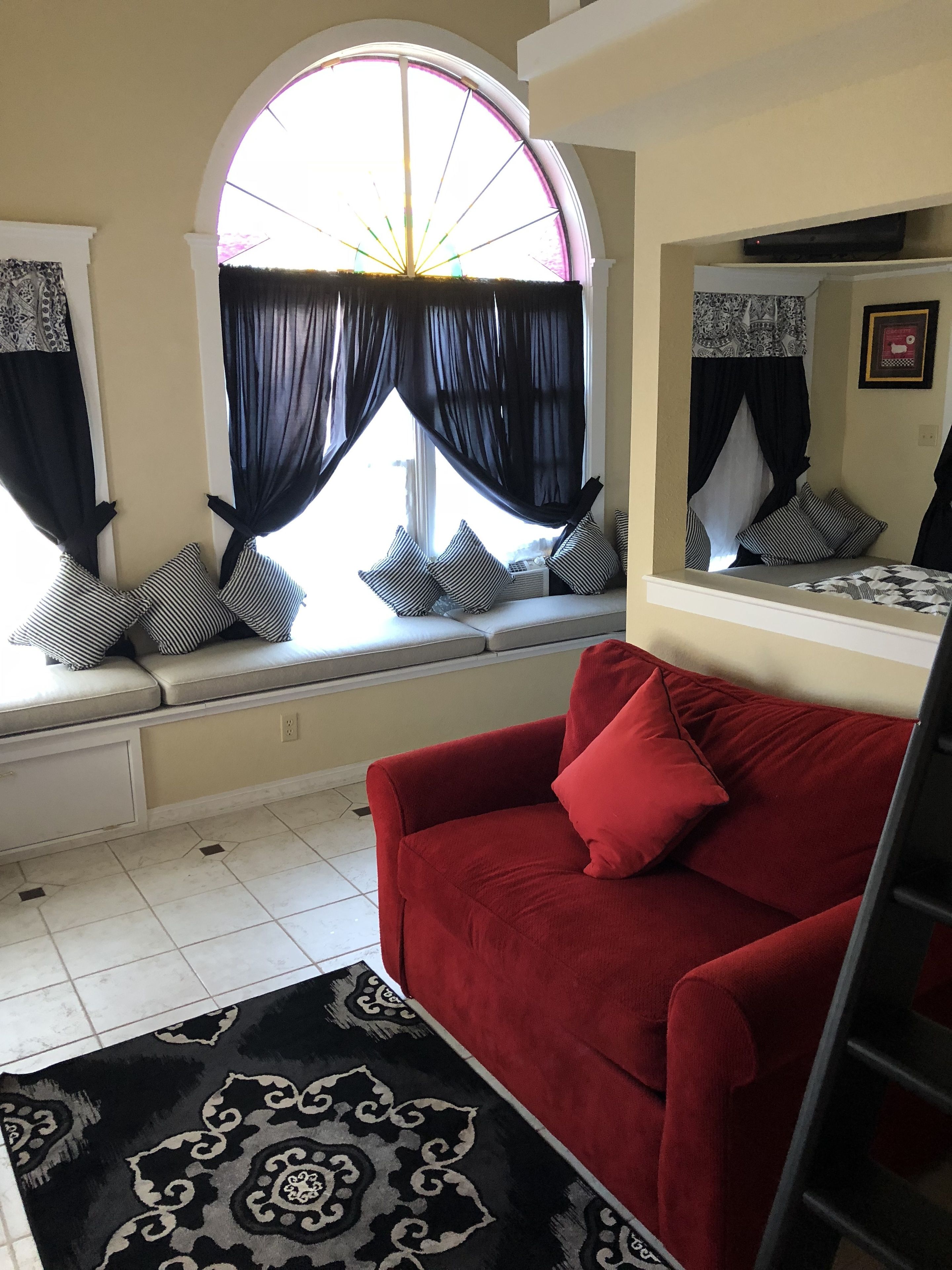 A living room with a red sofa, black and white patterned rug, and a window with black curtains.