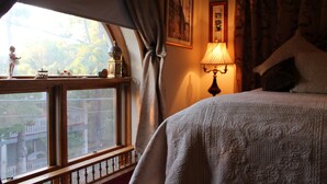 A bedroom with a bed, a window with curtains, a lamp, and a view of the outside. - All Seasons Inn (Eureka Springs)