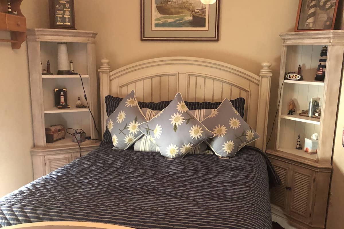 Quarto com cama, mesa de cabeceira, cômoda e relógio na parede.