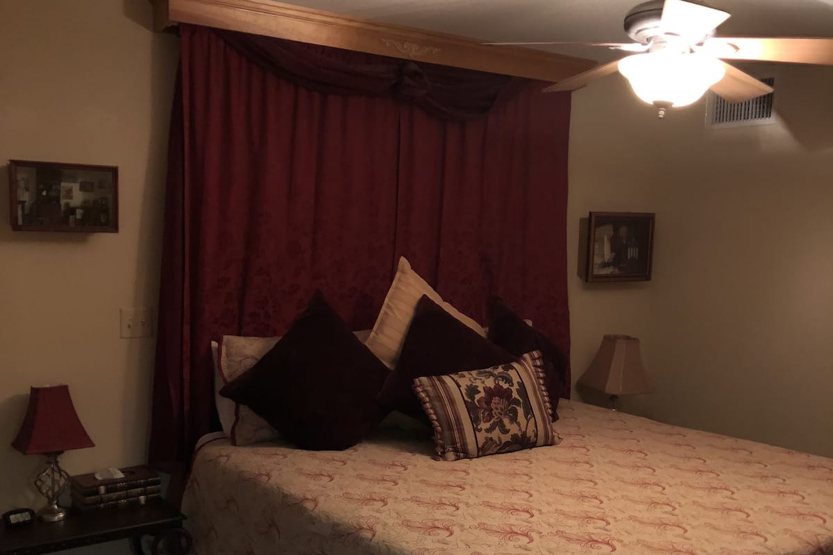 Quarto com cama, ventilador de teto e mesa de cabeceira com luminária.