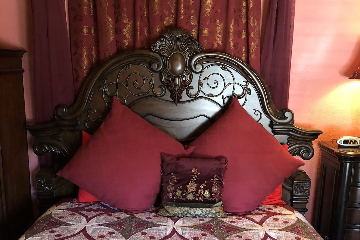 Uma cama com colcha estampada, cabeceira decorativa e almofadas vermelhas.