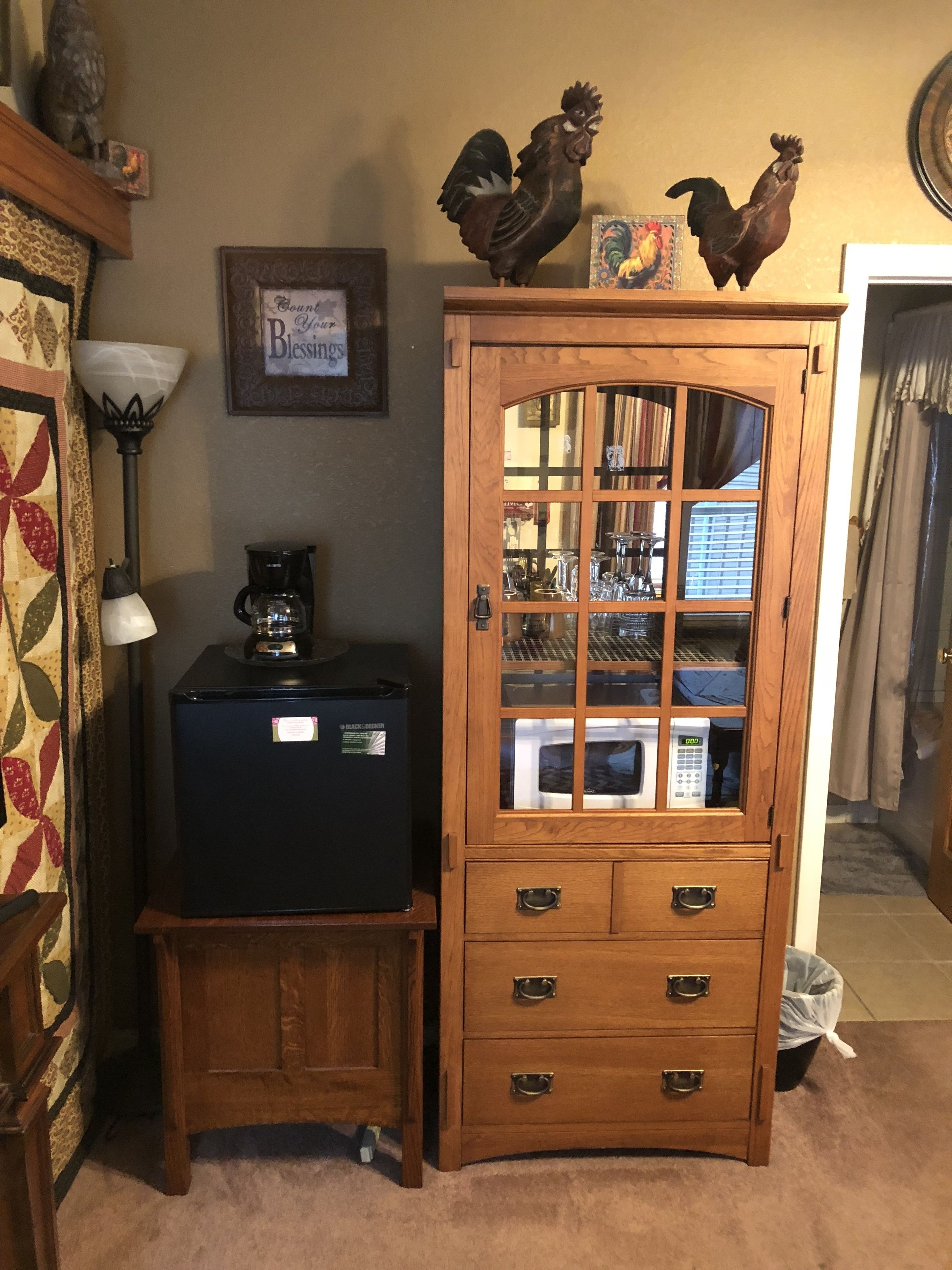 A wooden cabinet with glass doors, a coffee maker, and decorative rooster figures on top.