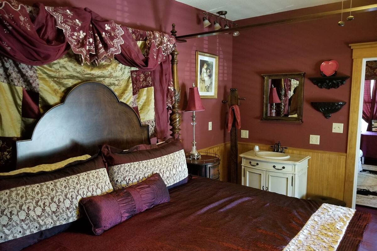 Quarto com cama grande, mesa de cabeceira, espelho e toucador com pia.