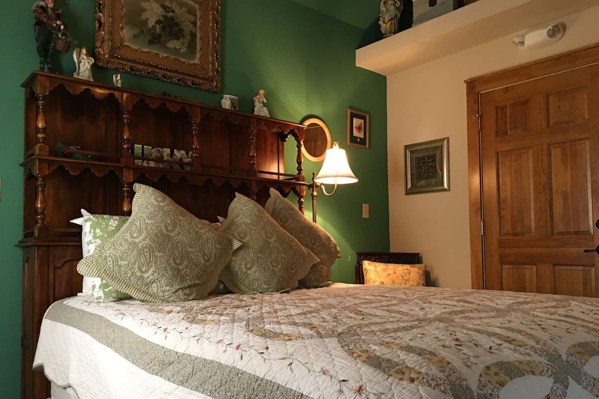 Quarto com cama grande, cômoda de madeira, espelho e parede verde.