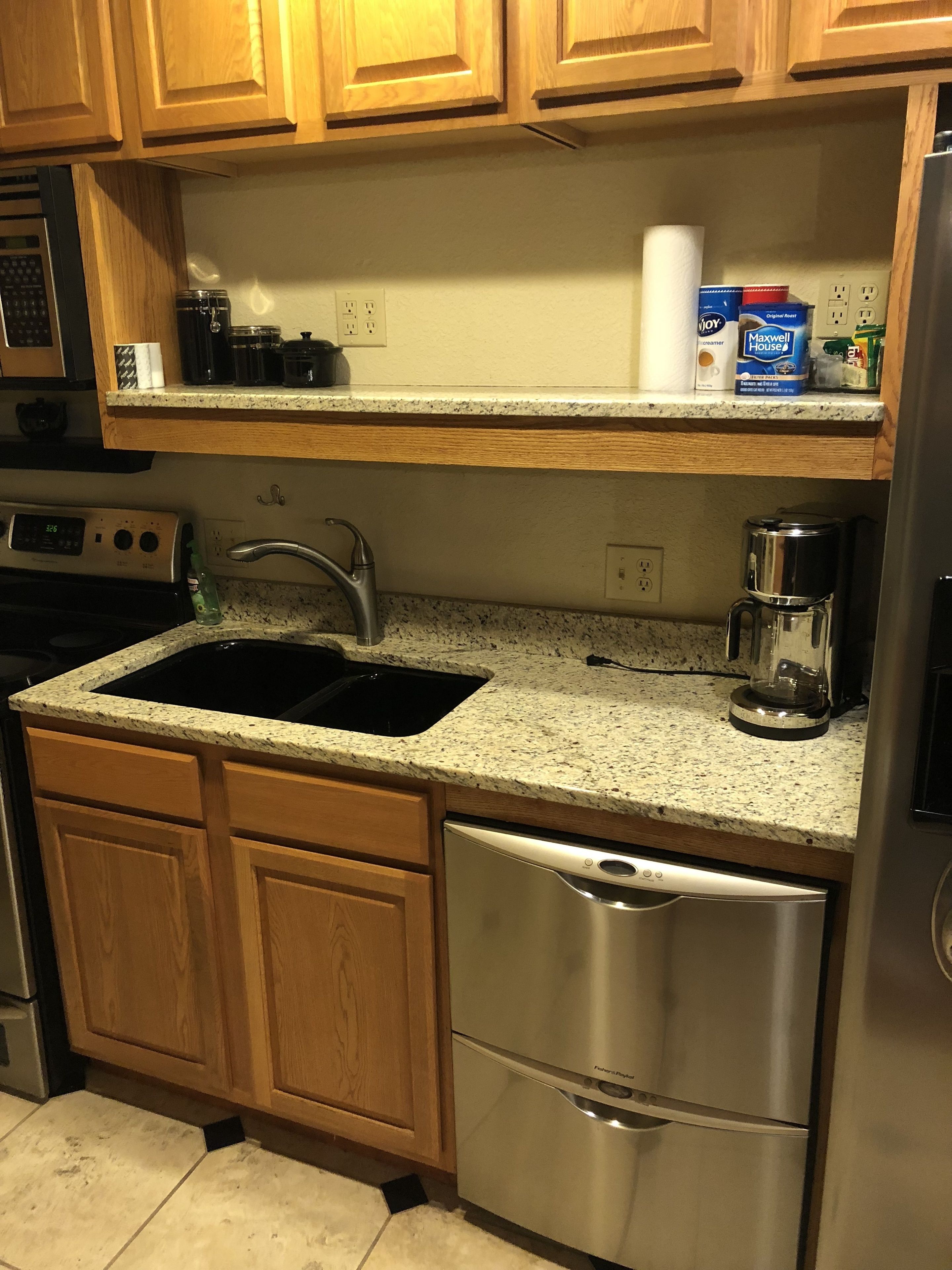 A kitchen with wooden cabinets, a stainless steel dishwasher, a double sink, and a coffee maker.