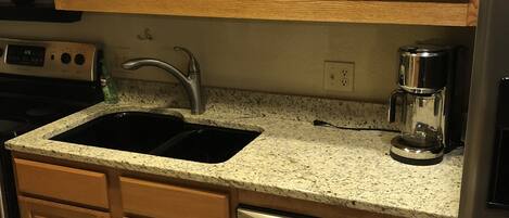 A kitchen with wooden cabinets, a stainless steel dishwasher, a double sink, and a coffee maker.