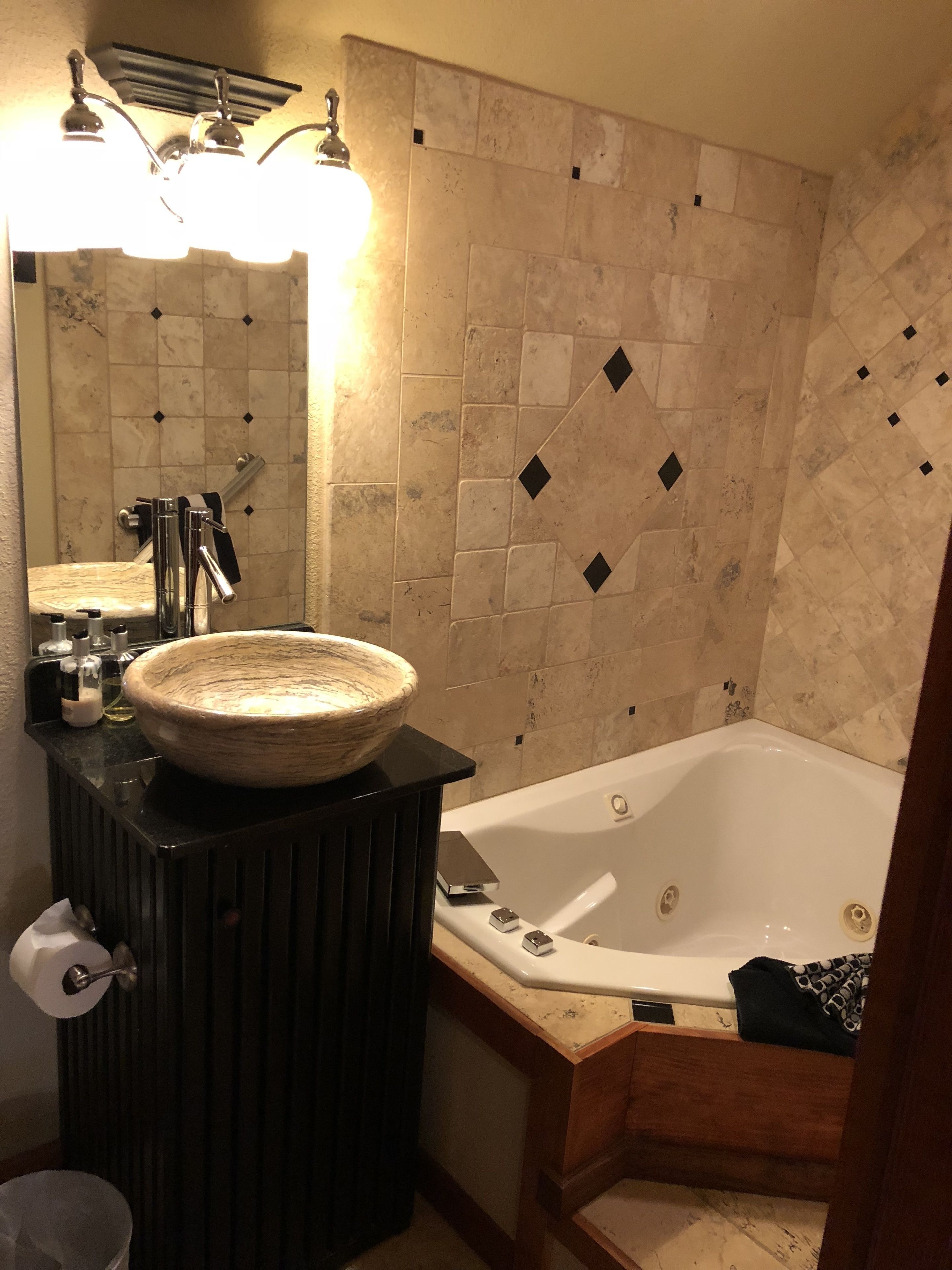 A bathroom with a large bathtub, a round sink, and a mirror above the sink.