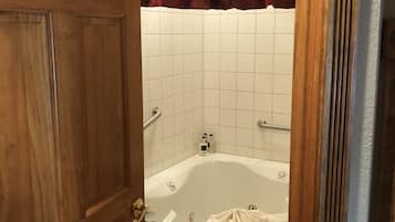 Un baño con puerta de madera, bañera blanca y cortina roja.
