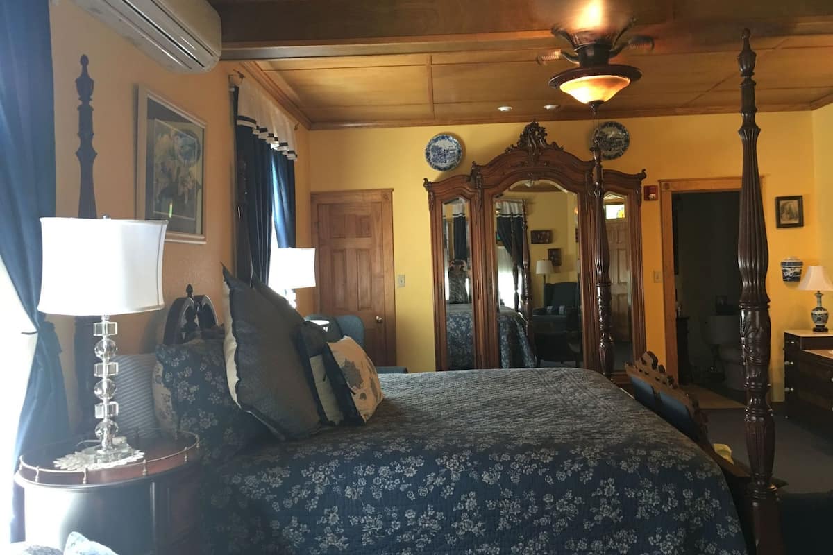 Quarto com uma cama, mesa de cabeceira com abajur, um espelho grande e ventilador de teto.