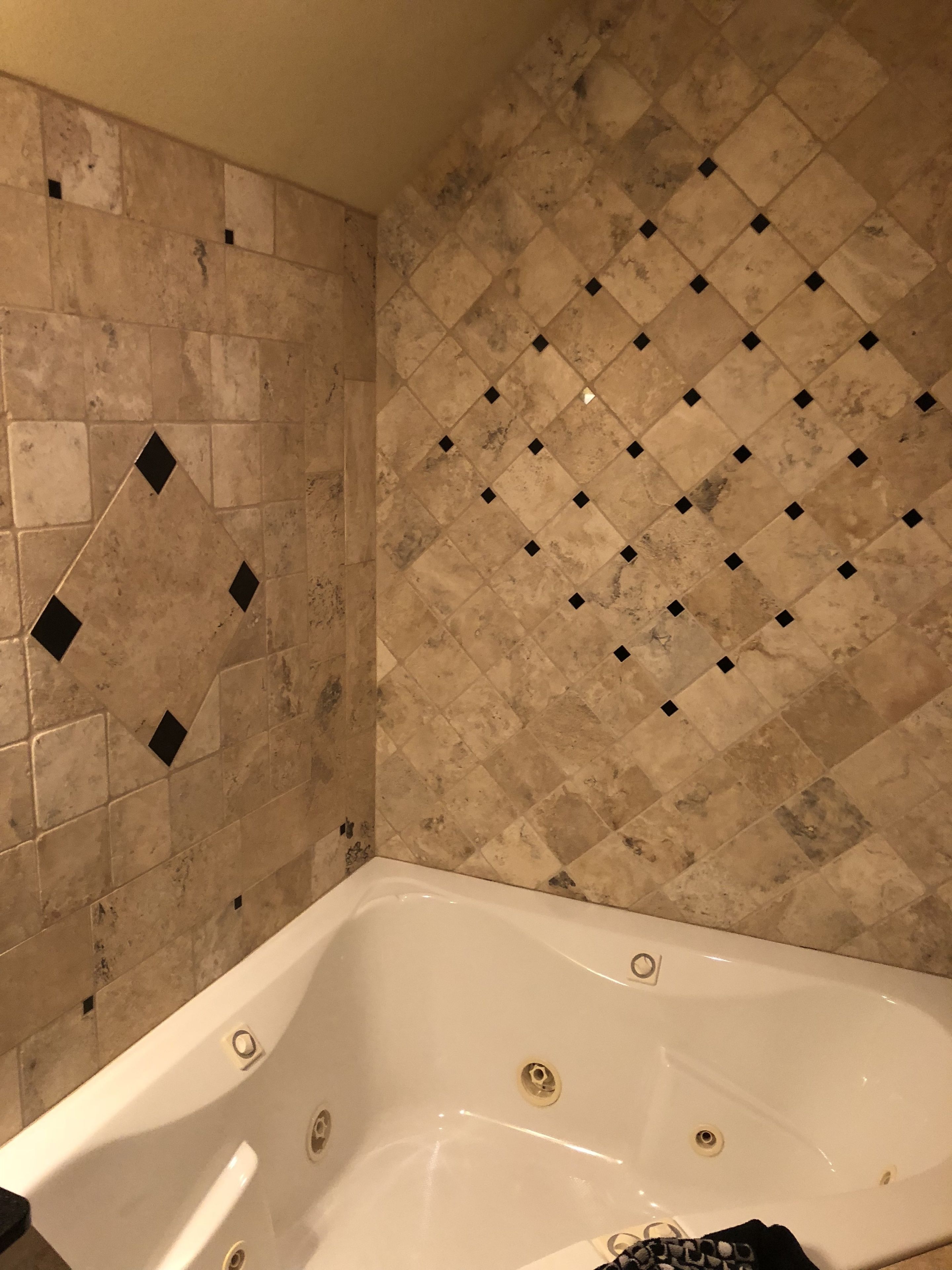 Un baño con bañera, paredes con azulejos color crema y diseño de mosaico en forma de rombo.