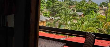 A balcony with a red floor, two wooden chairs, and a view of greenery and buildings.