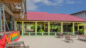 Un edificio frente a la playa con techo rojo, paredes verdes y asientos al aire libre.