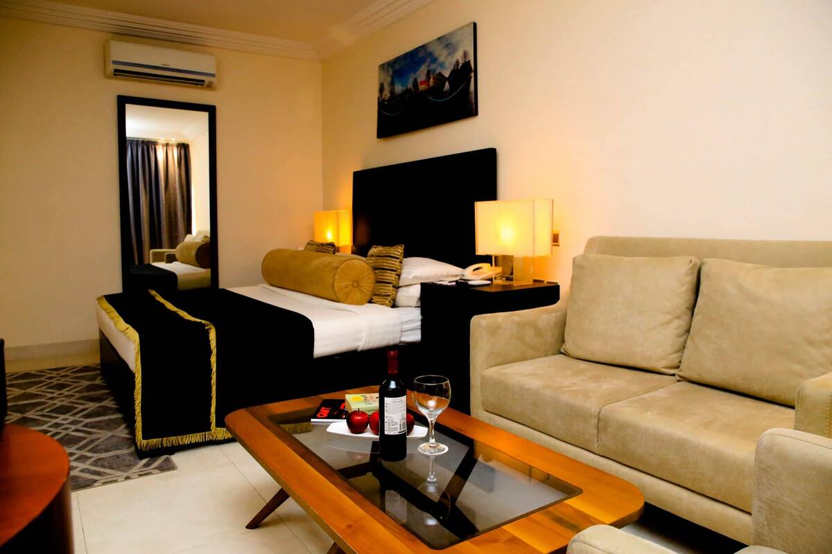 Ein Hotelzimmer mit Bett, einer Couch, einem Couchtisch mit Flasche und Glas sowie einem Bild an der Wand.