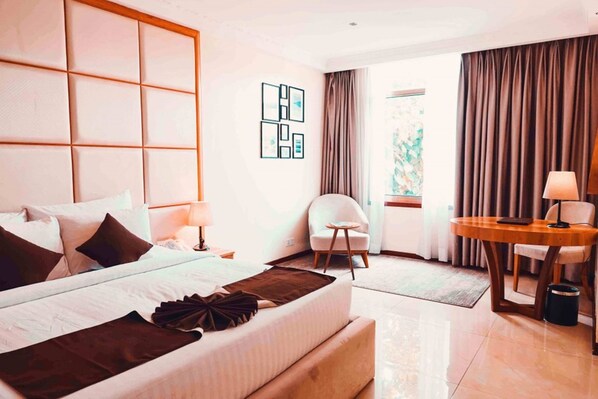 Habitación de hotel con una cama grande, un escritorio, una silla y vistas al exterior.