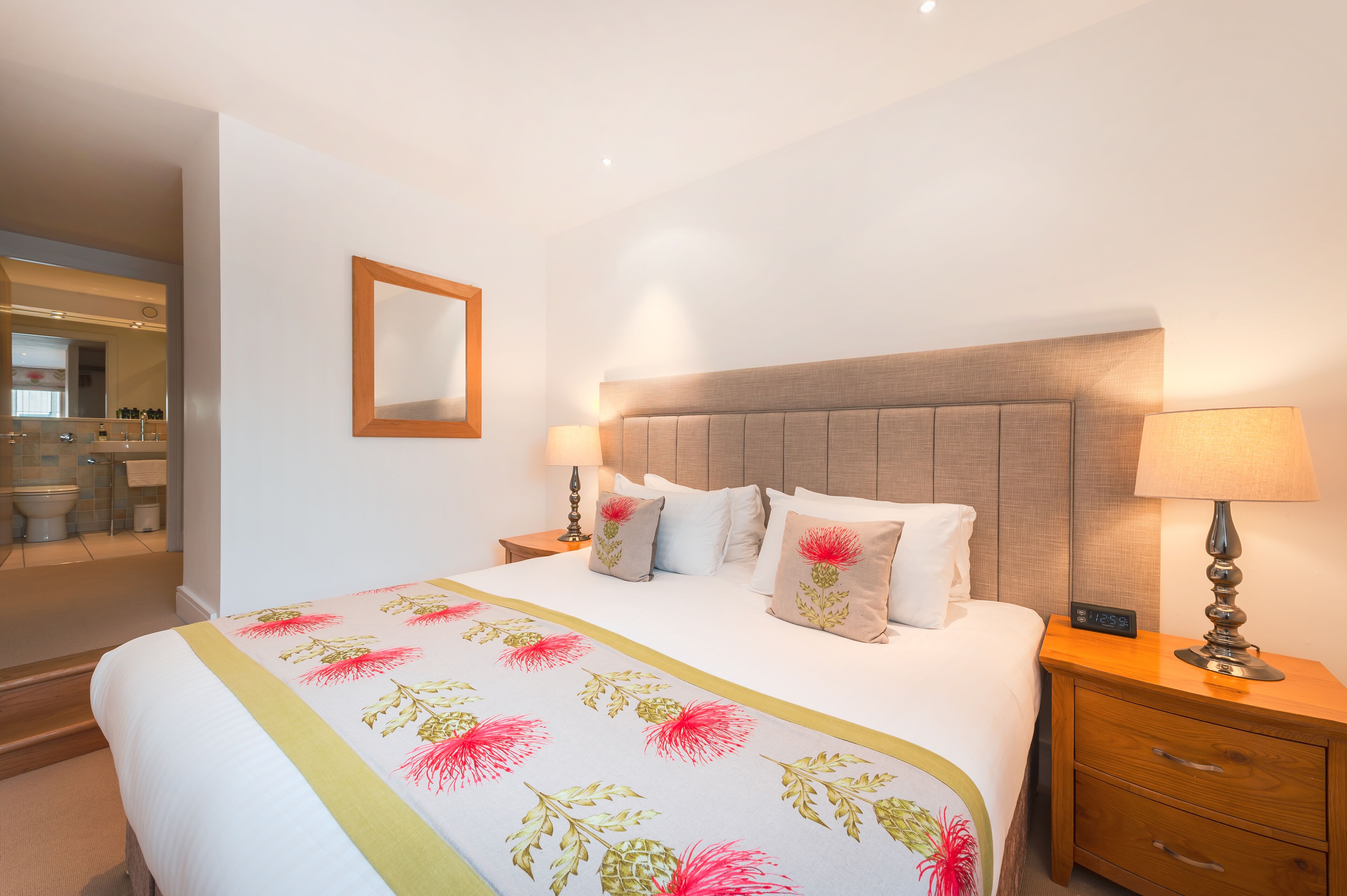Camera d'albergo con un letto grande, due comodini, uno specchio e un bagno visibile attraverso una porta aperta.