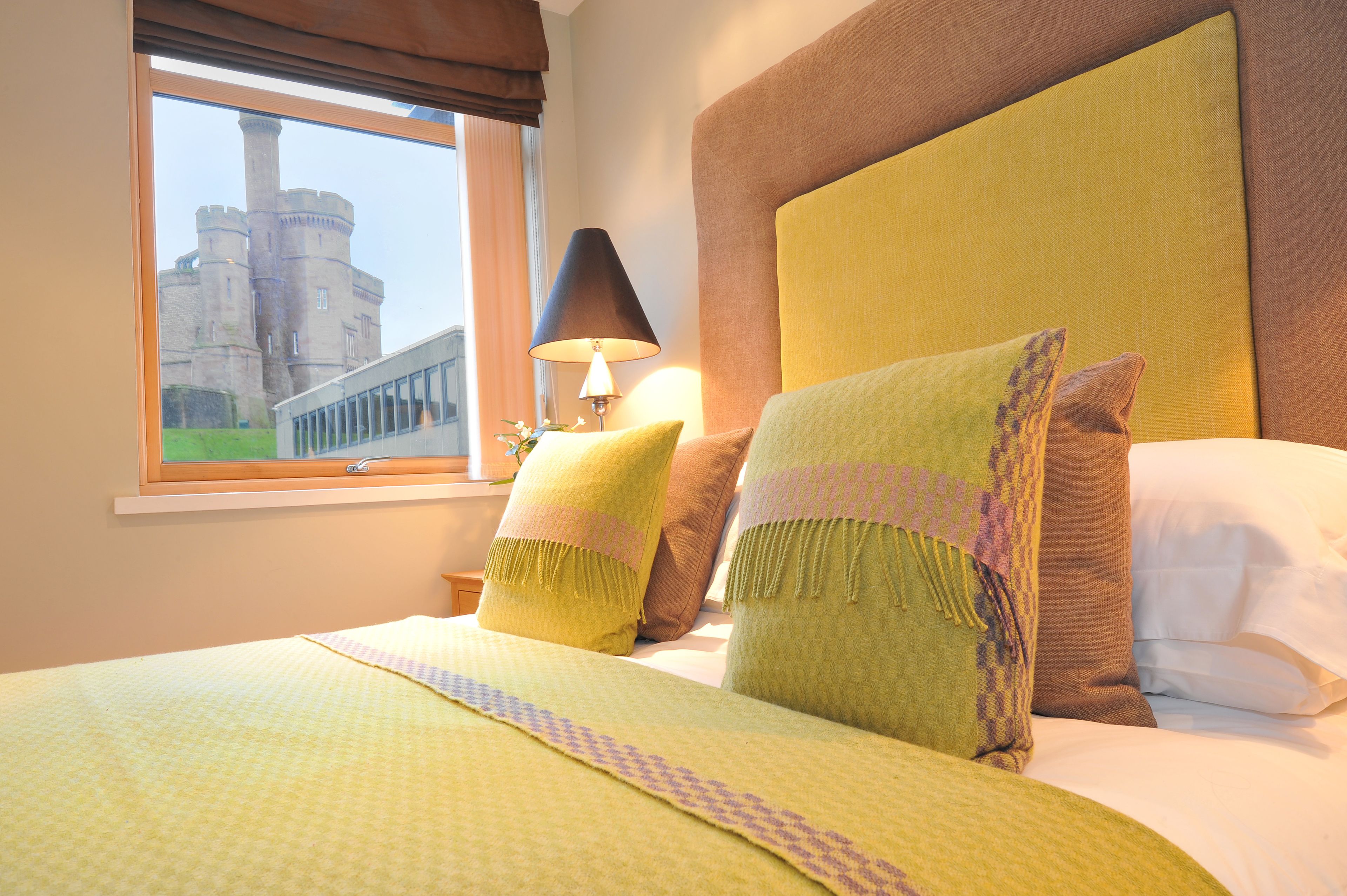 Un cuarto de hotel con una cama grande, una ventana que ofrece vistas a un castillo y una lámpara sobre una mesita de noche.