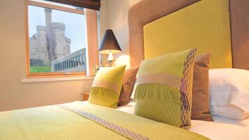Un cuarto de hotel con una cama grande, una ventana que ofrece vistas a un castillo y una lámpara sobre una mesita de noche.