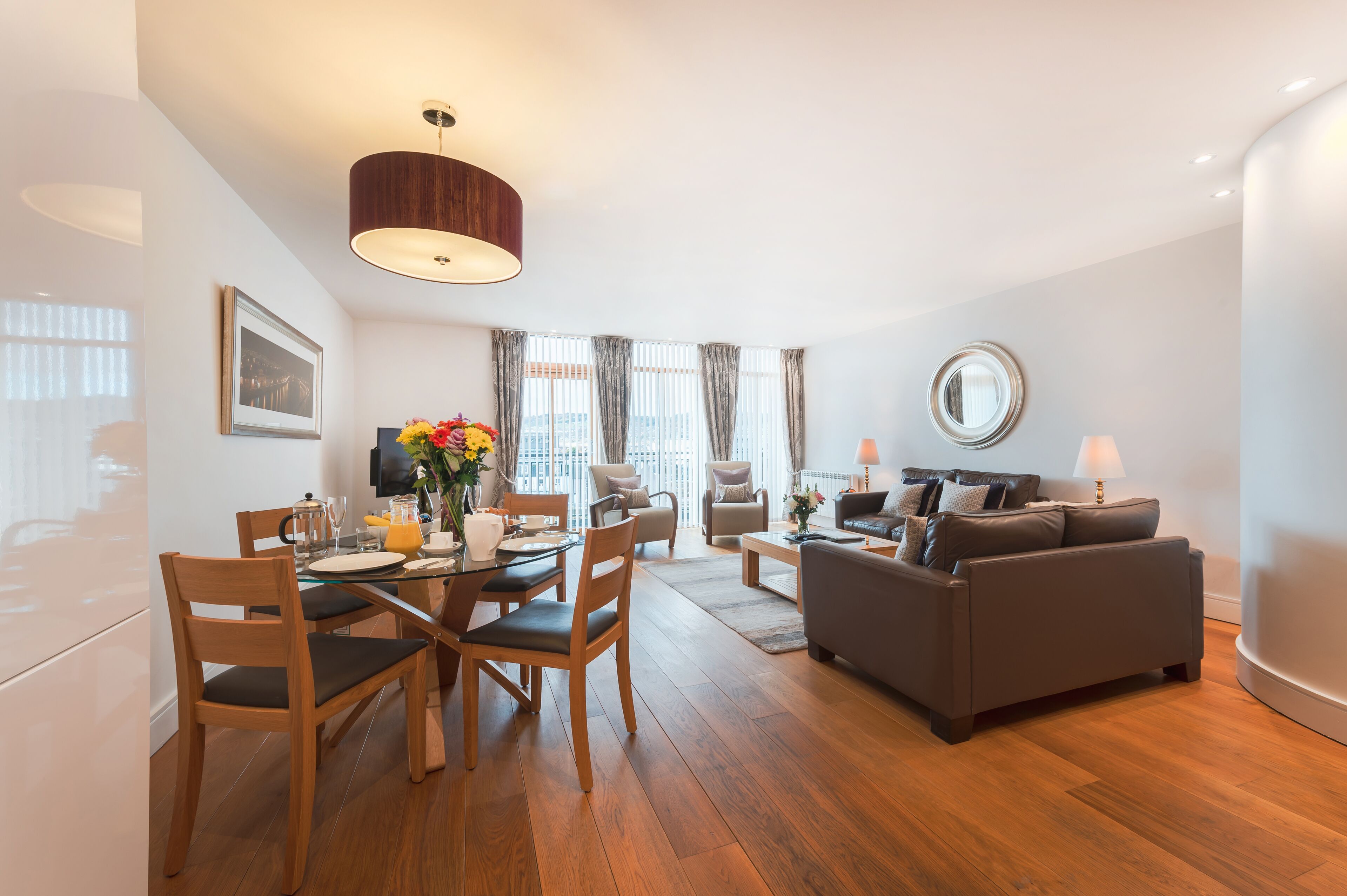 Una sala de estar moderna con comedor, que presenta piso de madera, un sofá gris, una mesa de centro y una mesa de comedor con sillas.