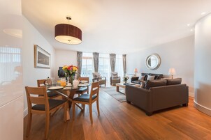 Una sala de estar moderna con comedor, que presenta piso de madera, un sofá gris, una mesa de centro y una mesa de comedor con sillas.