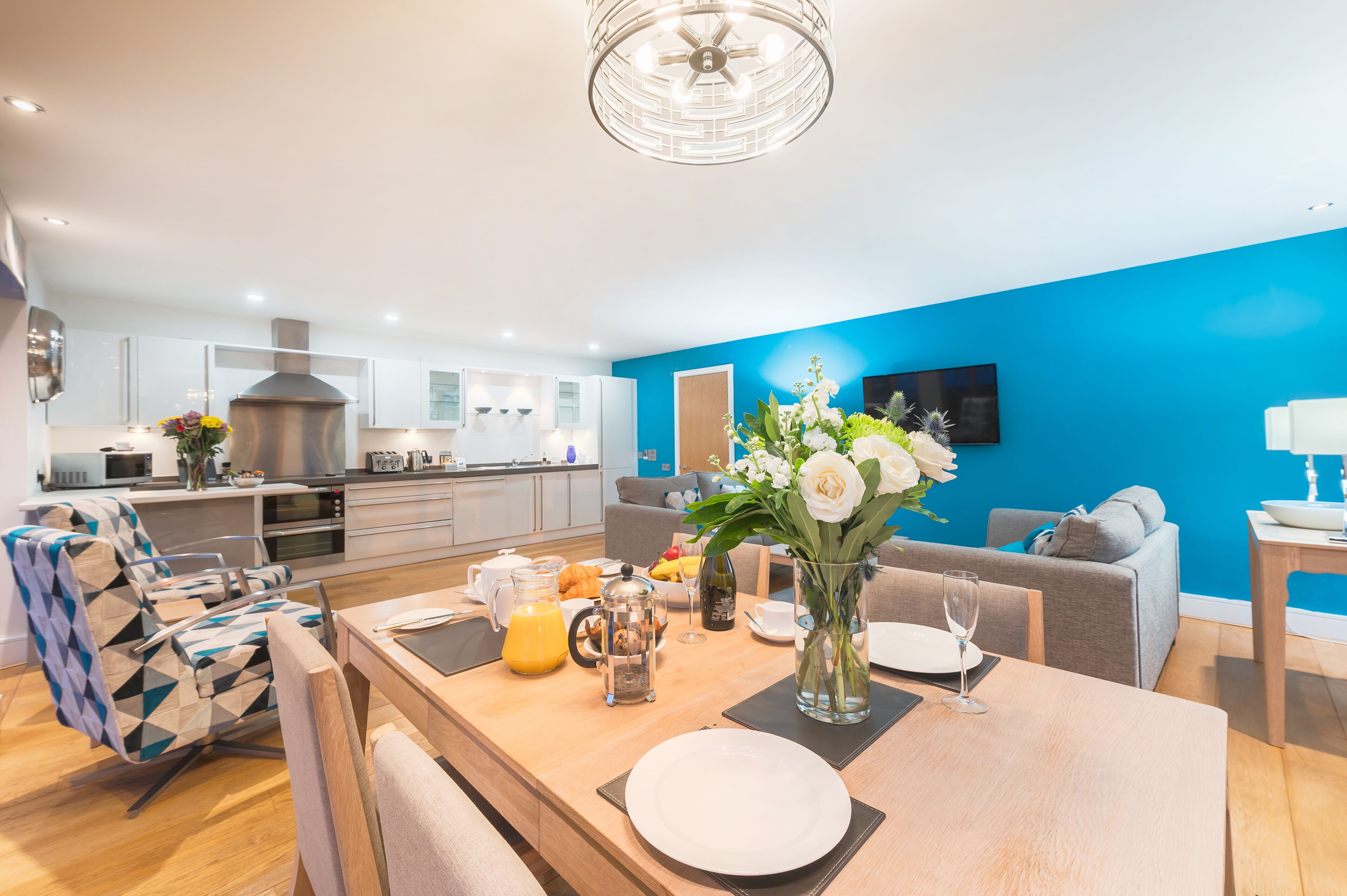 A modern kitchen with white cabinets, a stainless steel range hood, and a dining area with a wooden table set for breakfast.