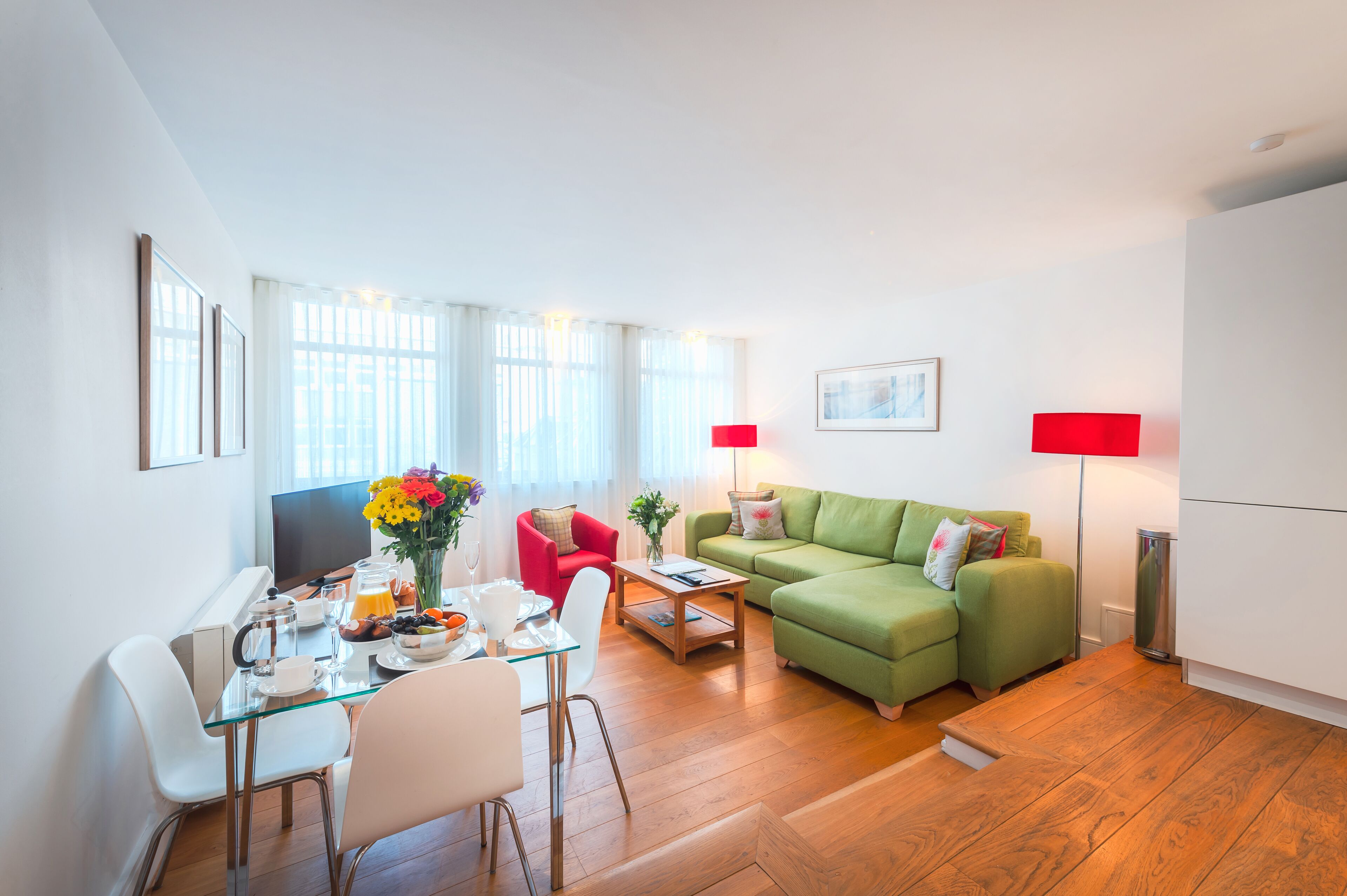Una sala de estar moderna con una mesa de comedor de vidrio, un sofá verde y una lámpara de pie roja.