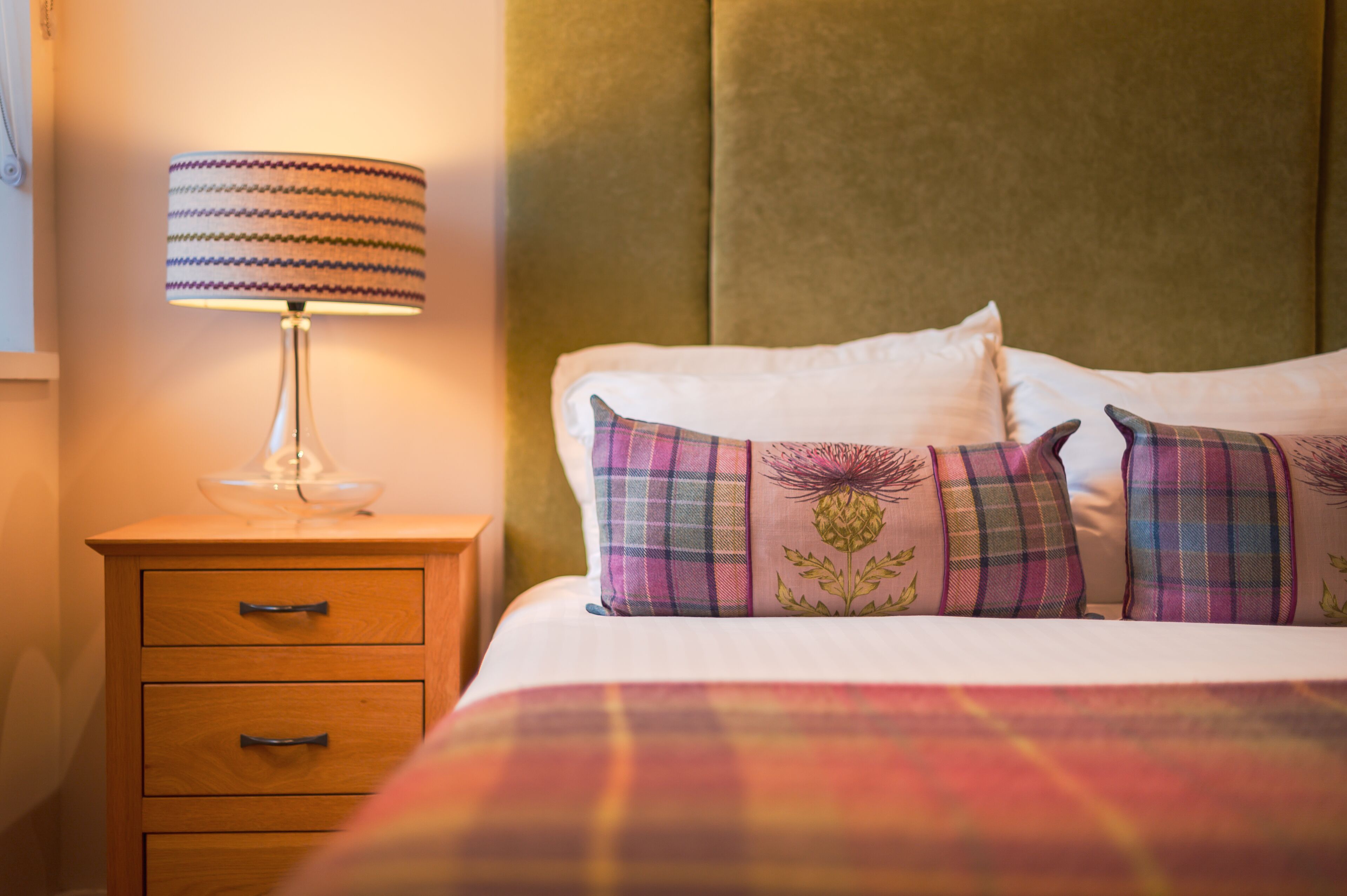 A neatly made bed with plaid pillows and a lamp on a wooden nightstand.