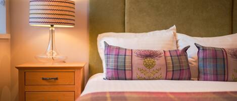 A neatly made bed with plaid pillows and a lamp on a wooden nightstand.