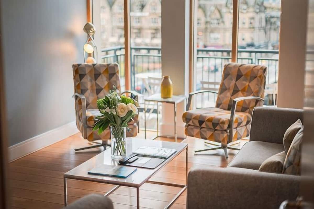 Un espace détente moderne avec des fauteuils à motifs, une table basse et un vase rempli de fleurs.