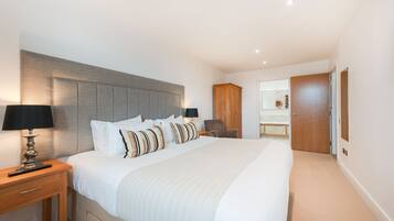 A modern bedroom with a large bed, bedside tables, a wooden wardrobe, and a bathroom visible through an open door.