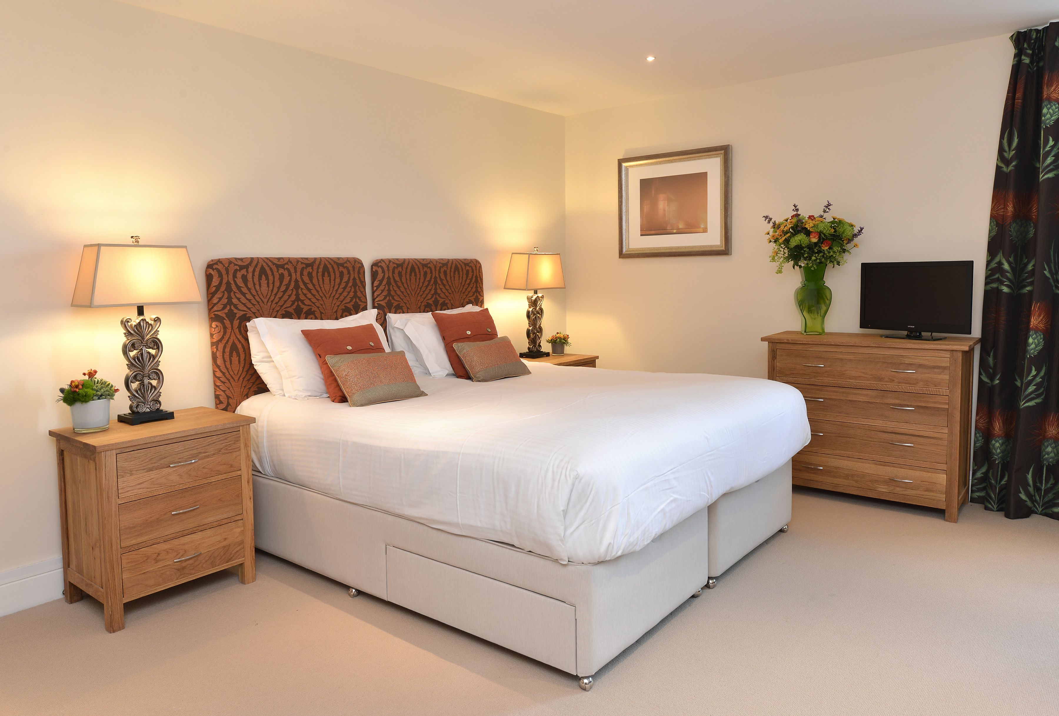 Une chambre à coucher bien rangée, avec un grand lit, deux tables de chevet avec des lampes, une télévision et une commode.