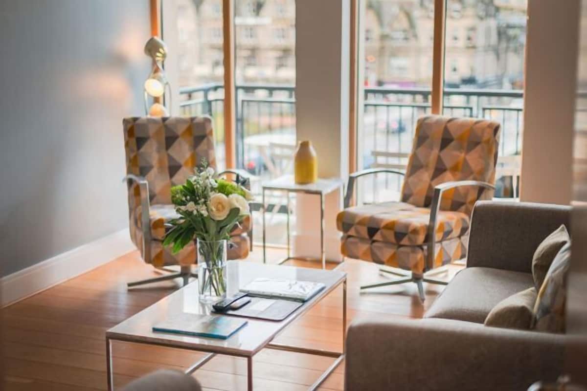 Un espace détente moderne avec des fauteuils à motifs, une table basse et un vase de fleurs.