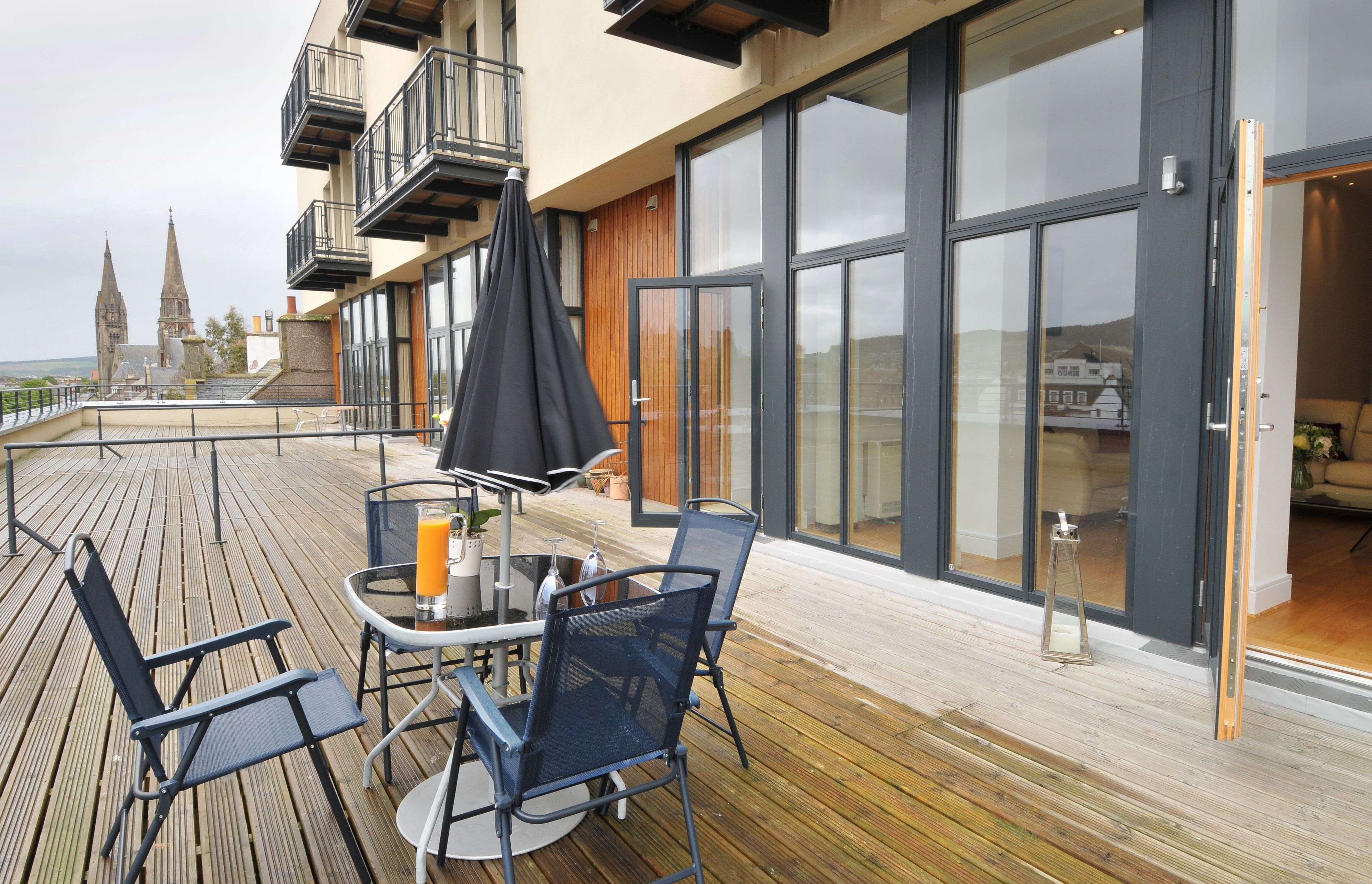 A deck with outdoor seating, a glass table, and a potted plant.