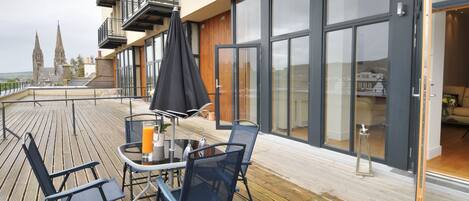 A deck with outdoor seating, a glass table, and a potted plant.