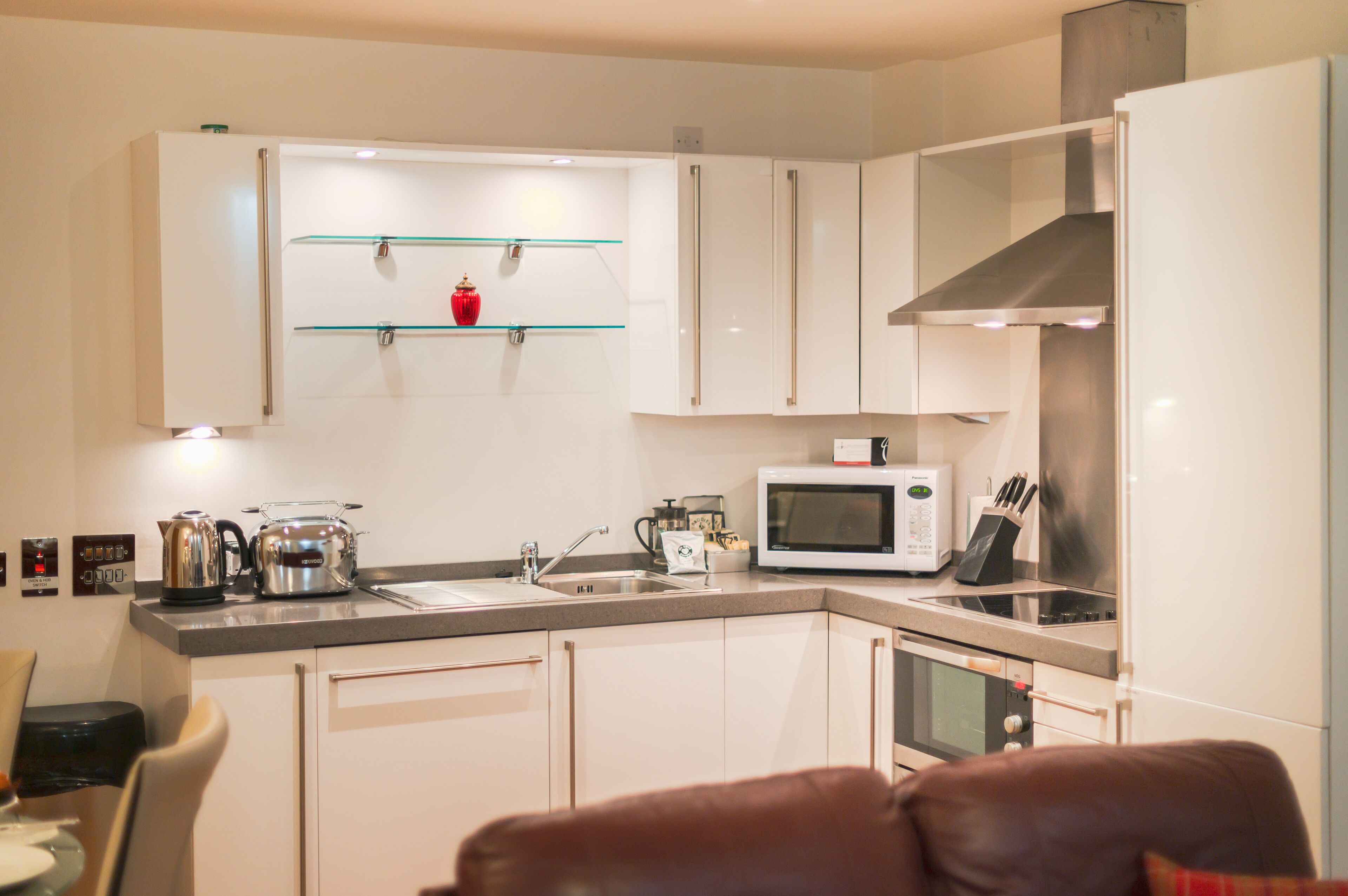 A modern kitchen with white cabinets, a stainless steel range hood, a microwave, and a kettle.