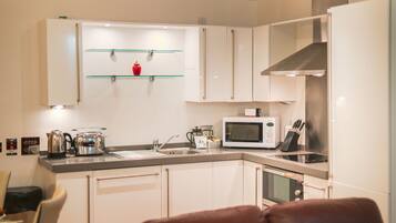 A modern kitchen with white cabinets, a stainless steel range hood, a microwave, and a kettle.