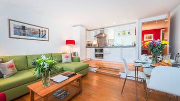 A modern living room with a green sofa, a coffee table, and a dining area with a glass table and chairs.
