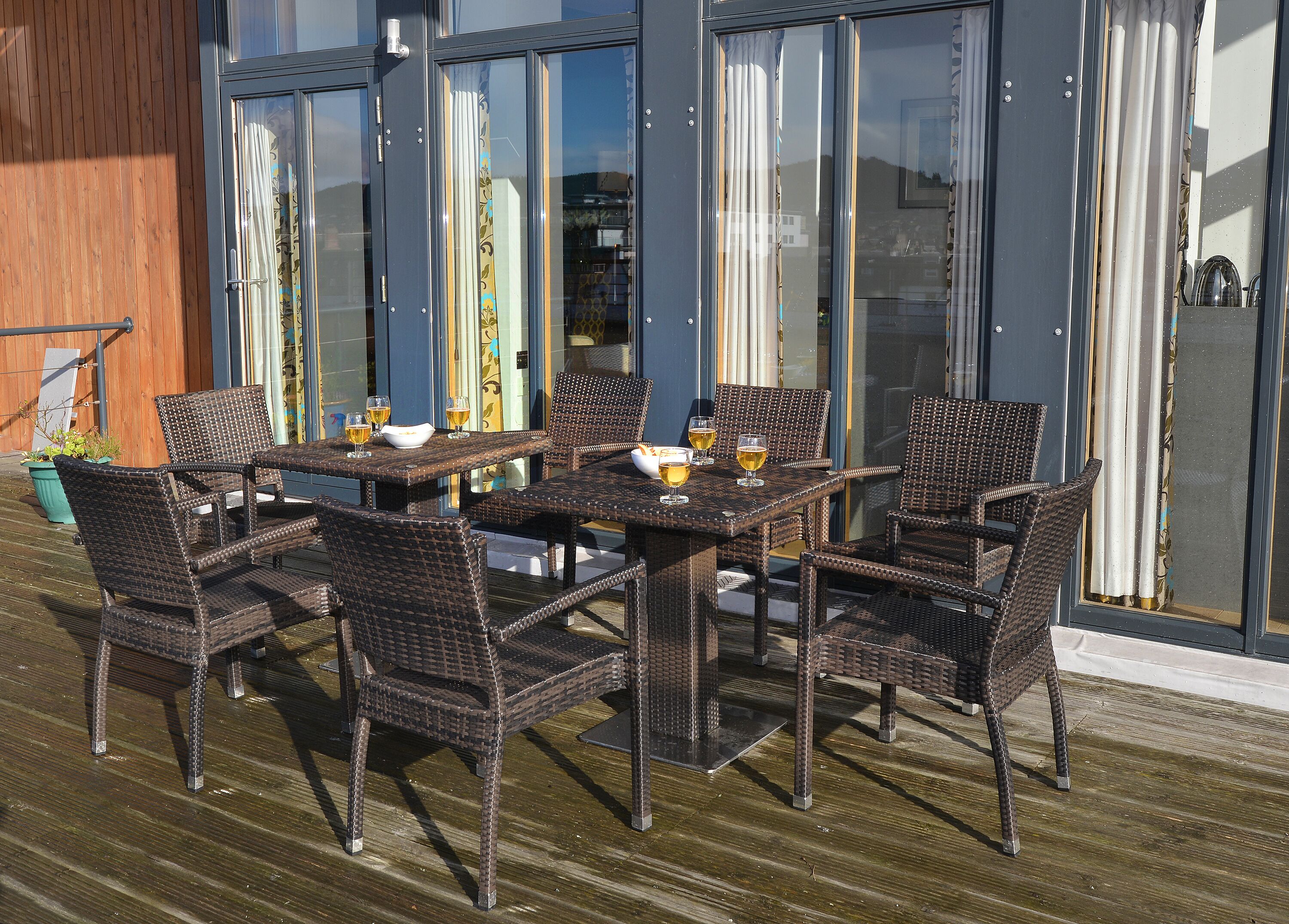 An outdoor dining area with wicker furniture and glassware on a wooden deck.