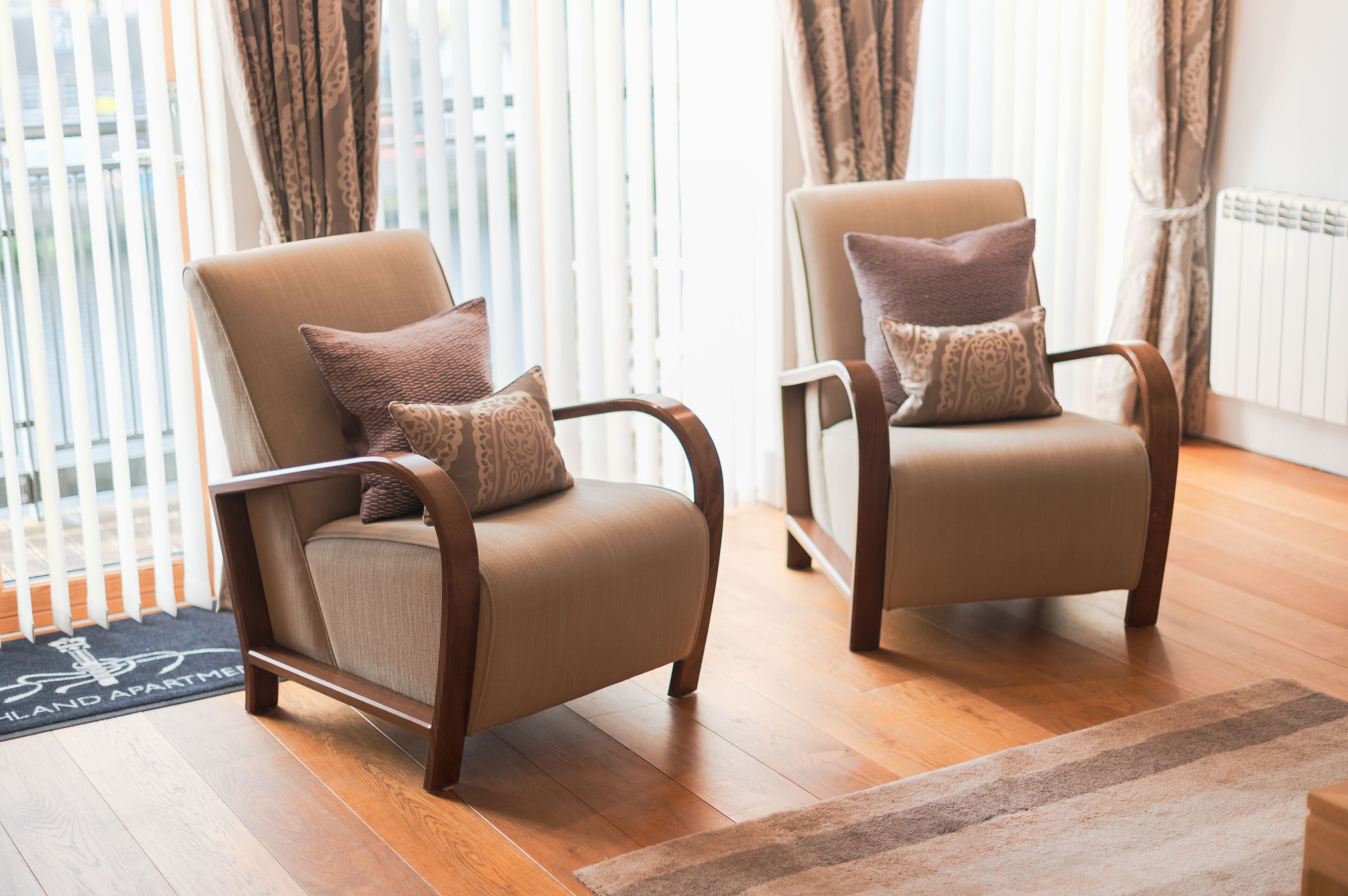 Two armchairs with patterned cushions in a room with wooden flooring and a view of a balcony.
