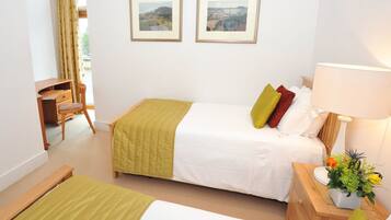 Een hotelkamer met twee bedden, een bureau, een stoel, een lamp en uitzicht op het buiten.