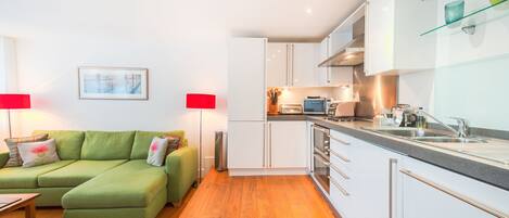 A modern apartment with a green sofa, a kitchen with white cabinets, and a dining area.