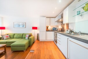 A modern apartment with a green sofa, a kitchen with white cabinets, and a dining area.