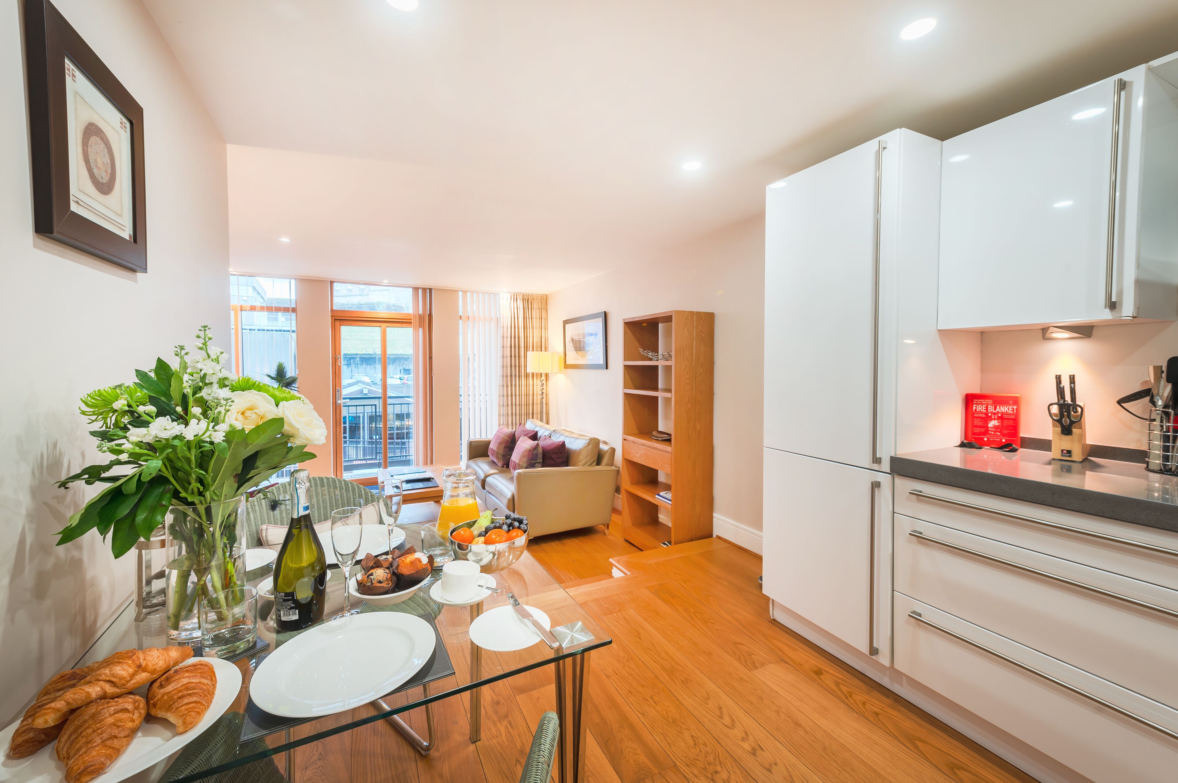 A modern kitchen with white cabinets, a dining table set with plates, a vase of flowers, and a bottle of wine.
