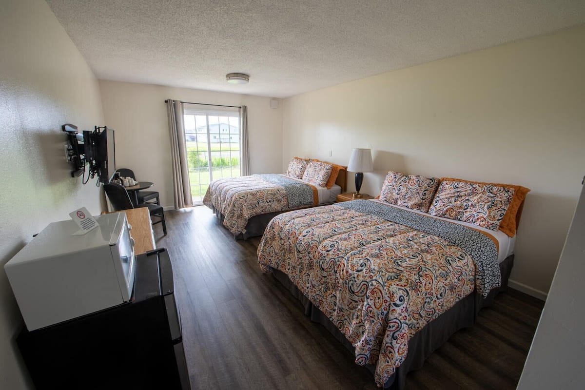 A hotel room with two beds, a desk with a computer, and a view of the outdoors.