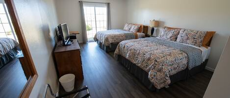 A hotel room with two beds, a desk, a chair, and a window with curtains.