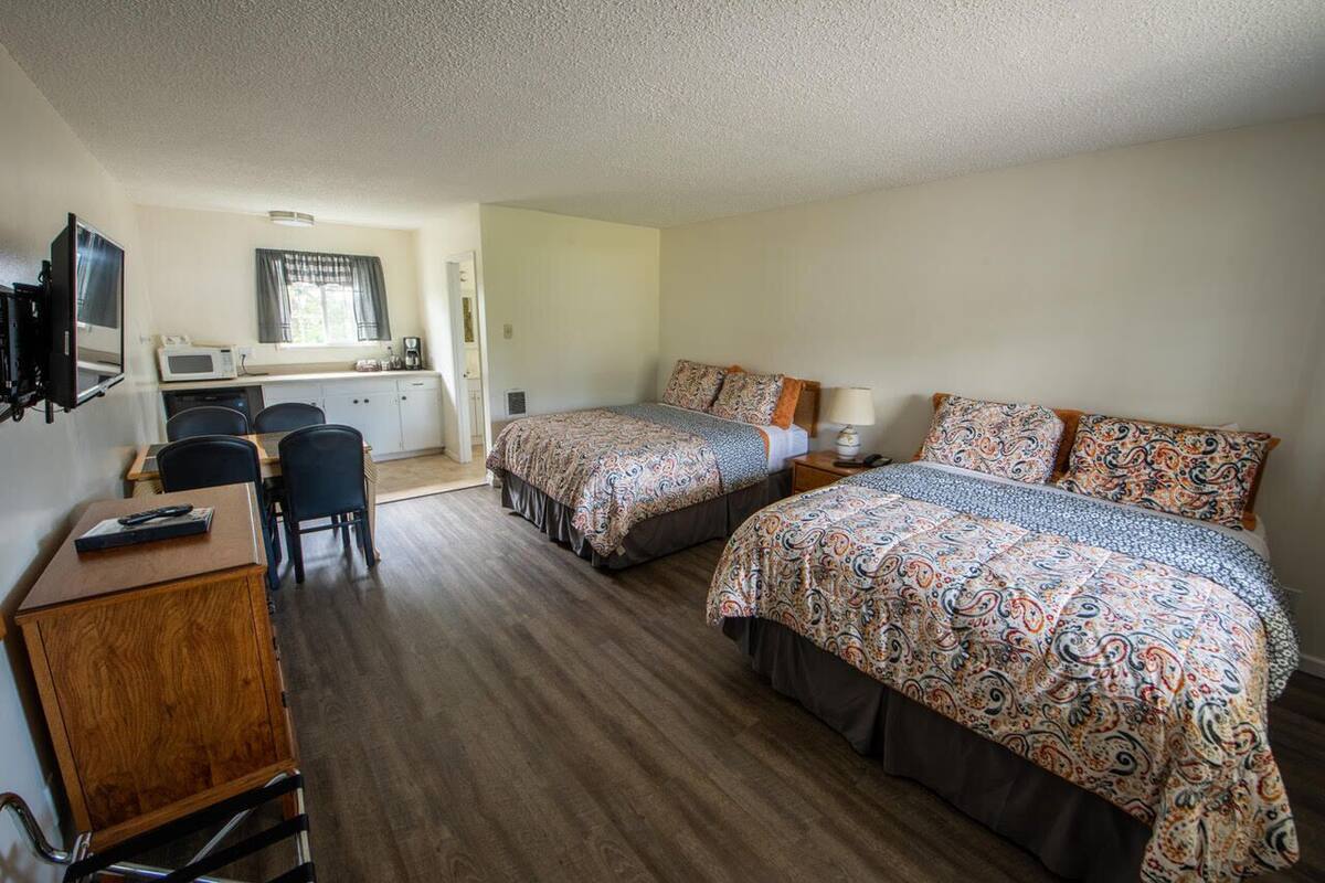 A compact hotel room with two beds, a kitchenette, a desk, and a TV.