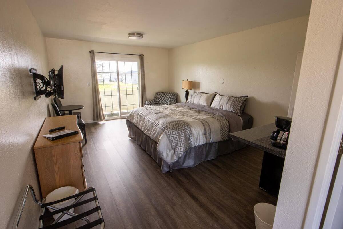A bedroom with a bed, a desk, a chair, a lamp, and a view through a window.