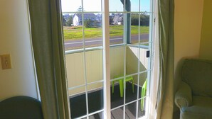 Une pièce donnant sur une route et des maisons, avec un fauteuil vert et une fenêtre avec des rideaux.
