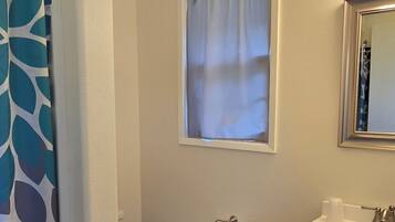 Un baño con inodoro, ventana con cortina, lavabo con espejo y cortina de ducha estampada con hojas.